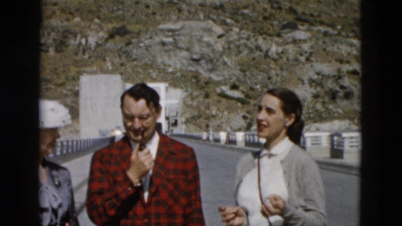 1958 Montana home-movie frame of adults on a sunny mountain road, including a man in a red plaid jacket and women beside him.
