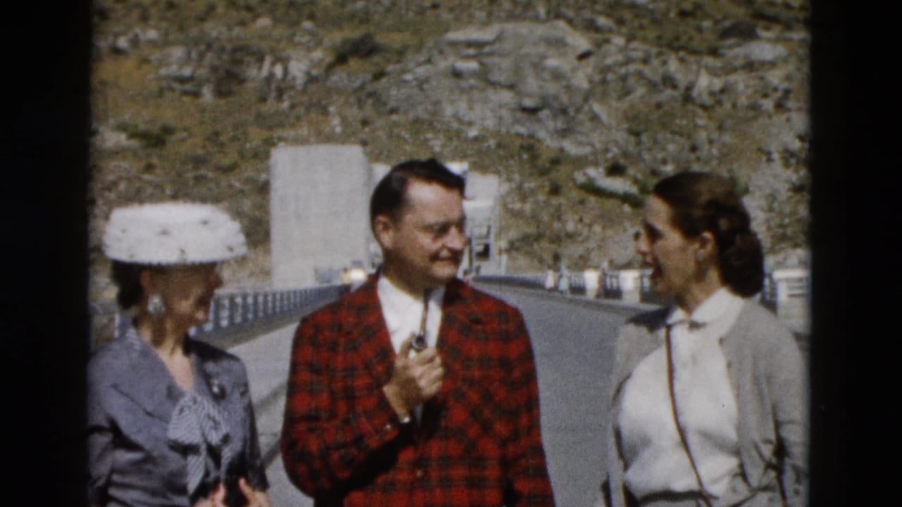 Three adults talking on a road with a rocky hillside behind them.