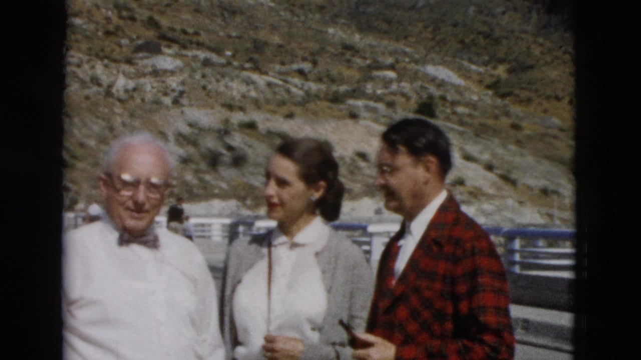 In 1958 Montana home-movie footage, an older man, a young woman, and a man in a red plaid jacket stand outdoors near a rocky hillside.
