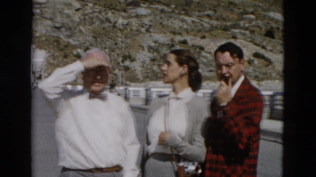 The older man shields his face from the sun as the woman and man in a red plaid jacket stand near a roadside railing in Montana.