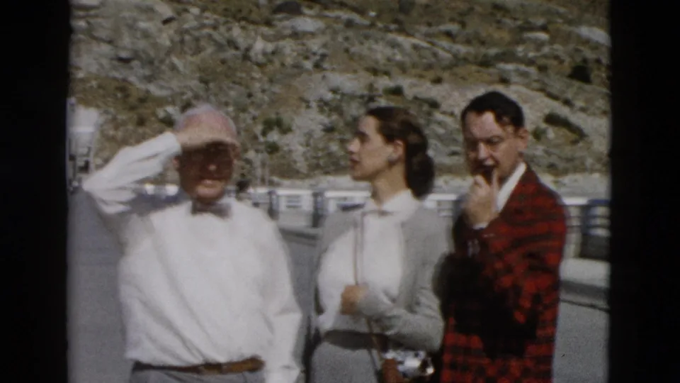 The older man shields his face from the sun as the woman and man in a red plaid jacket stand near a roadside railing in Montana.
