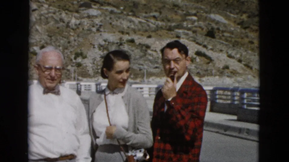 The older man, young woman, and plaid-jacketed man stand together in bright sun during a 1958 Montana roadside home movie.