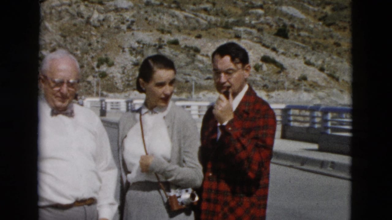 Three adults stand at an overlook with hills and railings behind them.