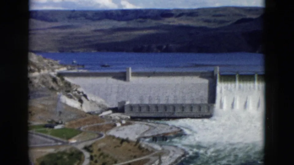The dam spillway releases white water beneath a blue reservoir in this 1958 Montana 8mm home-movie frame.