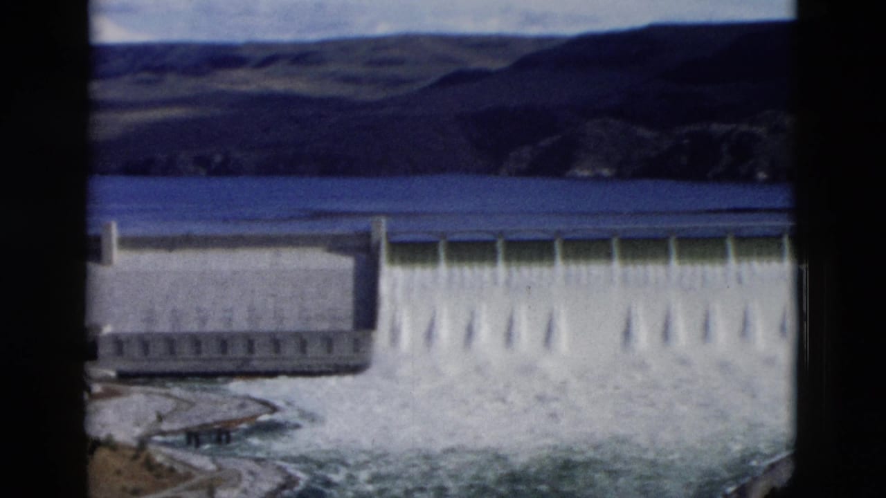 Wide view of dam spillway with white water pouring down the face.