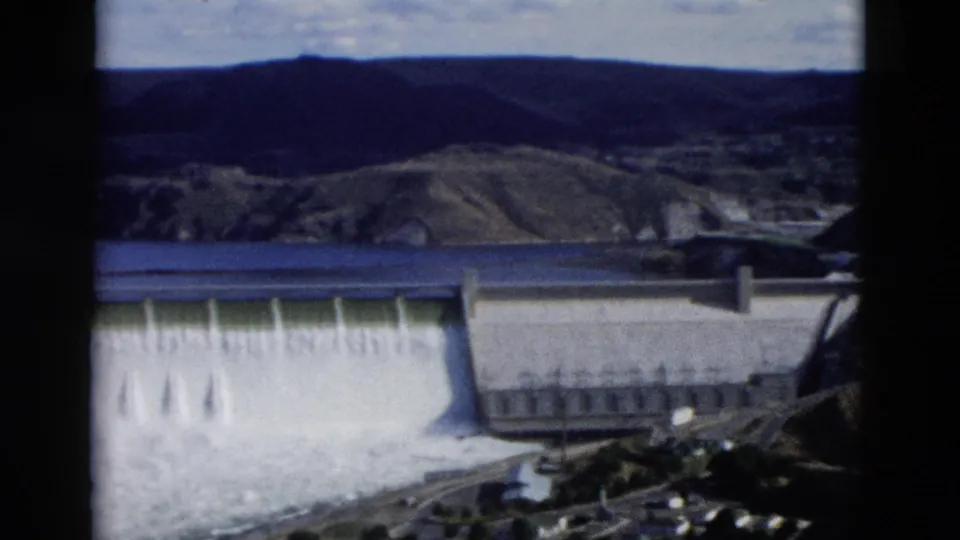 1958 Montana 8mm frame with a dam face, cascading spillway water, and a concrete building at the right side.