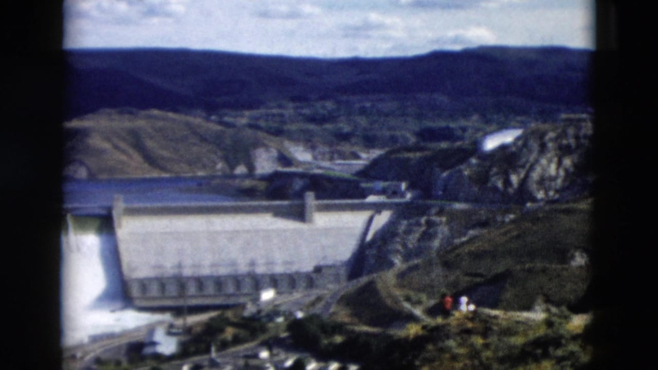 Large concrete dam with spillway water in a rocky mountain valley.