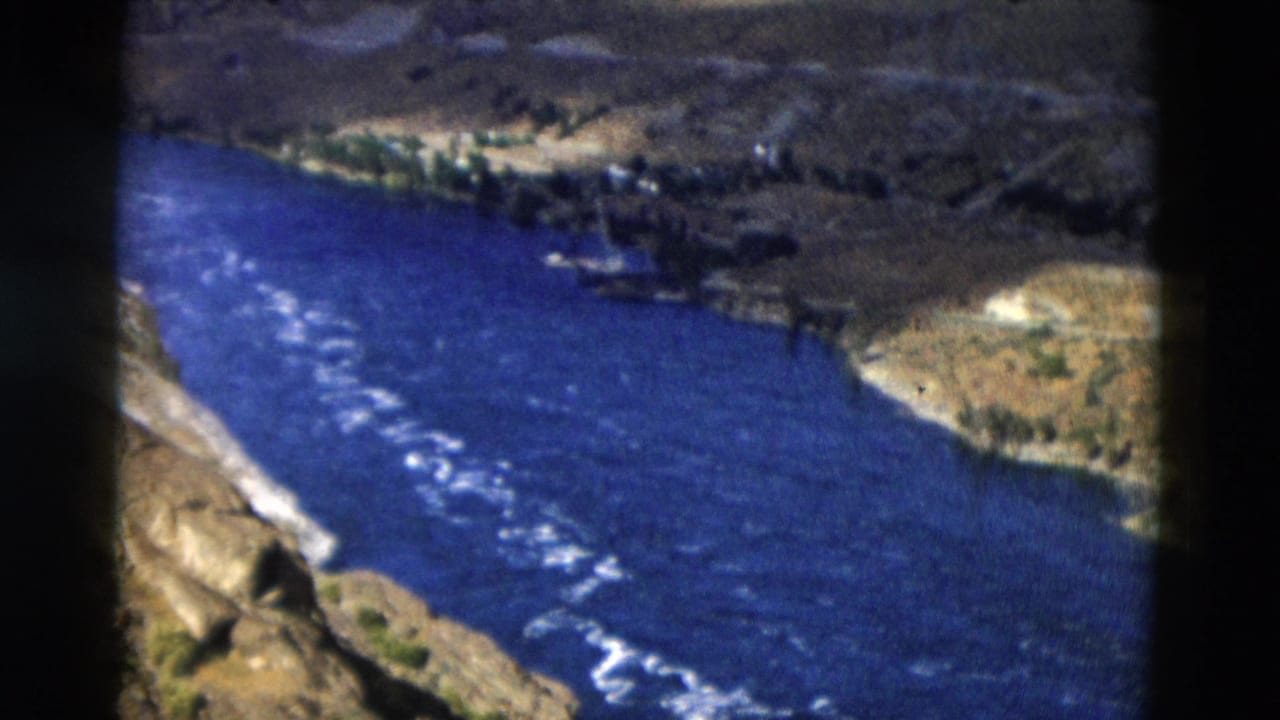 Blue river with white rapids cutting through dry mountain terrain.