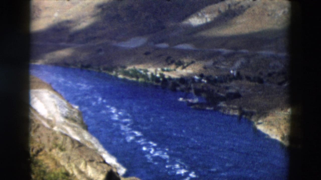 Aerial view of a blue river bend below shadowed hills.