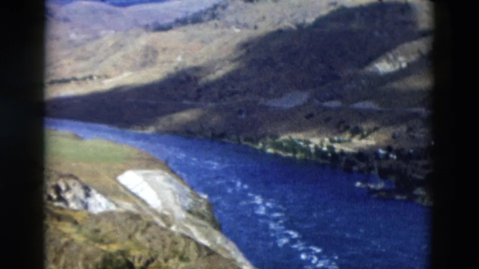 1958 Montana 8mm frame of a wide blue river beside a pale gravel bar and rough mountain slopes.