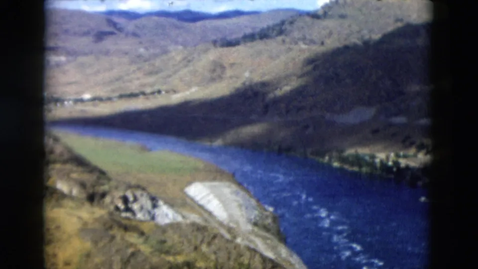 1958 Montana aerial view of the river continuing through a mountain valley, with rapids and a bright gravel bank visible below.