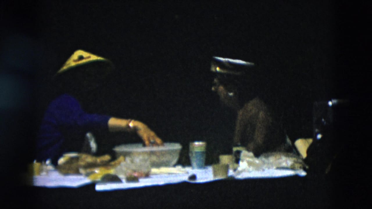 The women continue their outdoor meal, with a large bowl, paper cup, cooler, and bags visible against a dark wooded background.