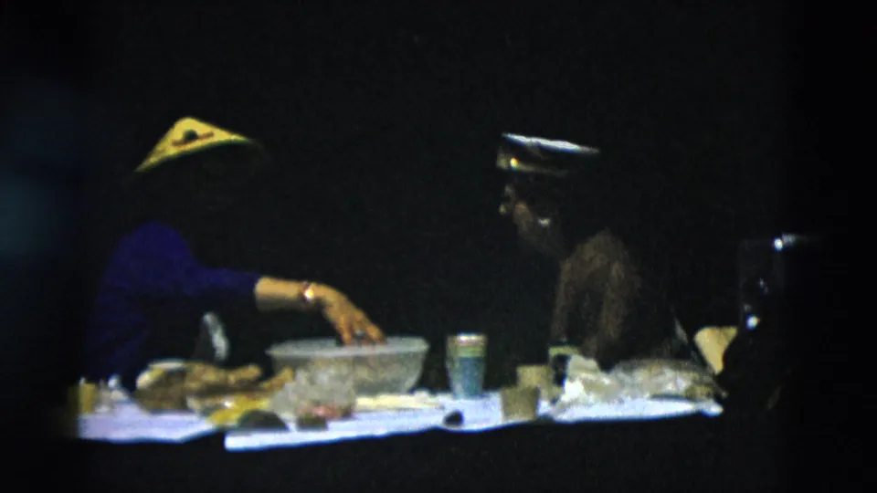 The women continue their outdoor meal, with a large bowl, paper cup, cooler, and bags visible against a dark wooded background.
