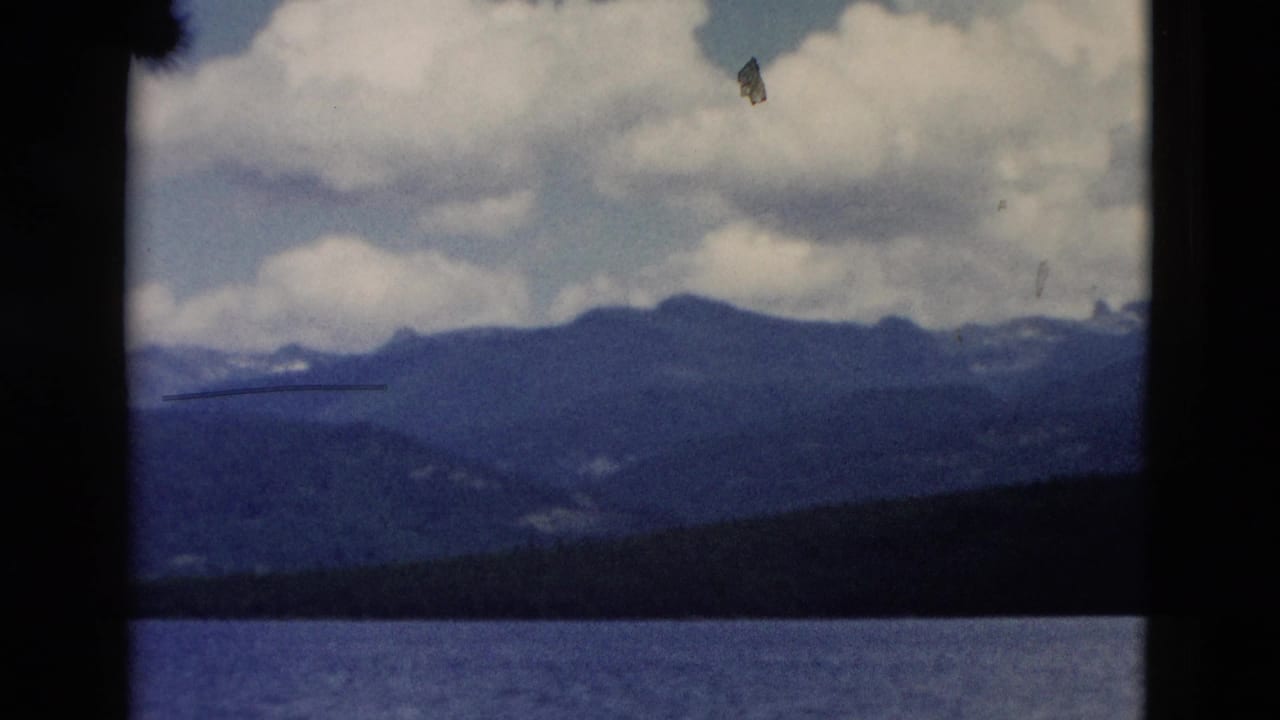 Lake, forested shoreline, distant blue mountains, and clouds seen through film-frame borders.