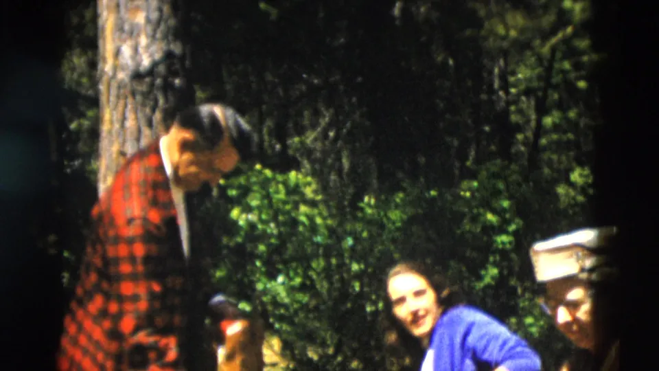 1958 Yellowstone picnic scene with adults seated or standing near trees, including one person in a red plaid jacket.
