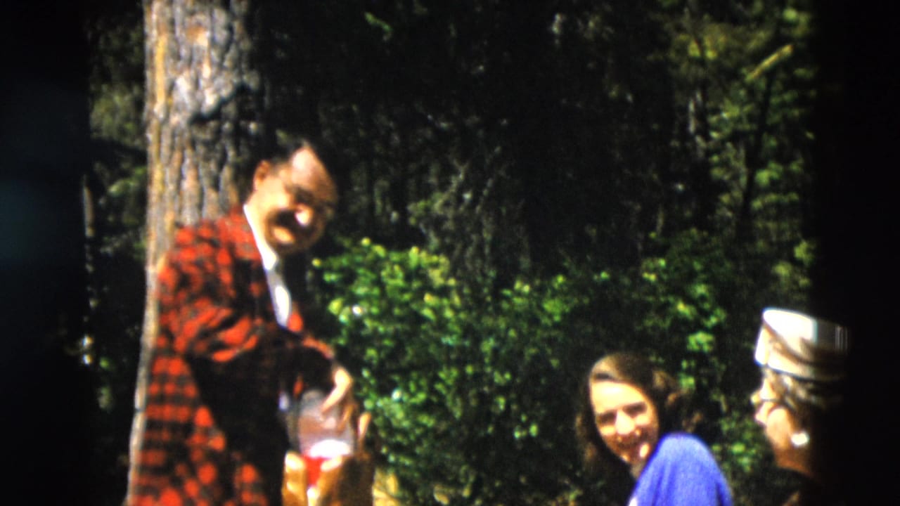 Man in plaid jacket stands beside two women in a shaded forest.