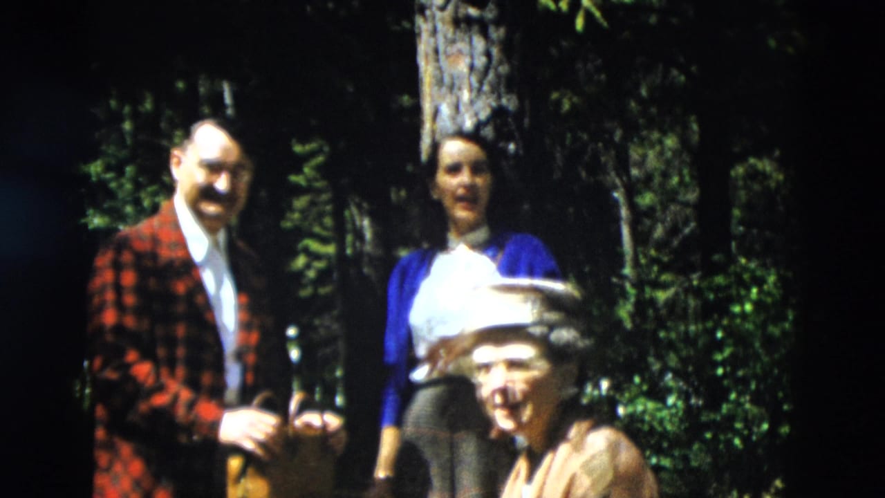 1958 Yellowstone home-movie frame showing family members in a wooded area, including a man in a plaid jacket and women near trees.