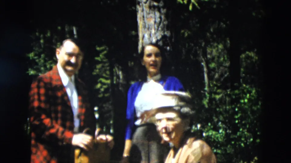 1958 Yellowstone home-movie frame showing family members in a wooded area, including a man in a plaid jacket and women near trees.