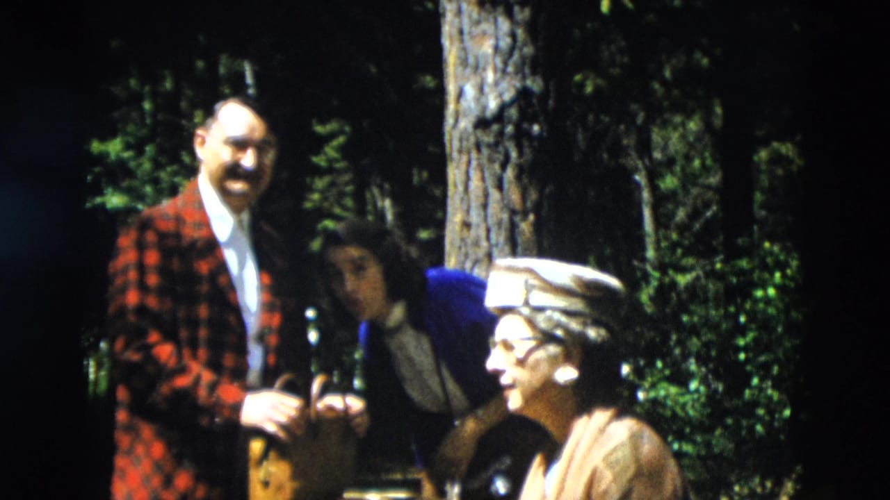 1958 Yellowstone frame with a man in a red plaid jacket, a woman leaning nearby, and an older woman seated in a hat among trees.