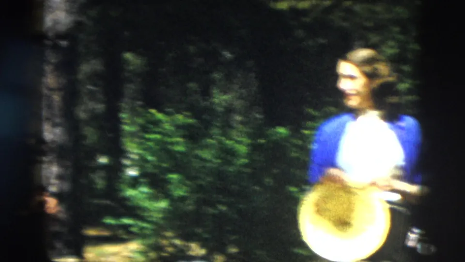 Woman in a blue cardigan holds a round straw-colored object while standing in a Yellowstone forest setting.