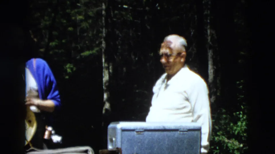 Older man in a white shirt stands near a metal cooler as part of the 1958 Yellowstone family forest outing.