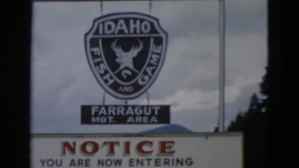 The Idaho Fish and Game shield remains centered as a notice board begins to enter the lower frame.