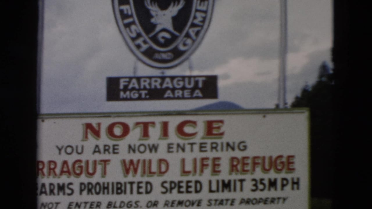1958 8mm frame of the Farragut Wild Life Refuge entrance notice, with Fish and Game emblem, trees, and cloudy sky visible.