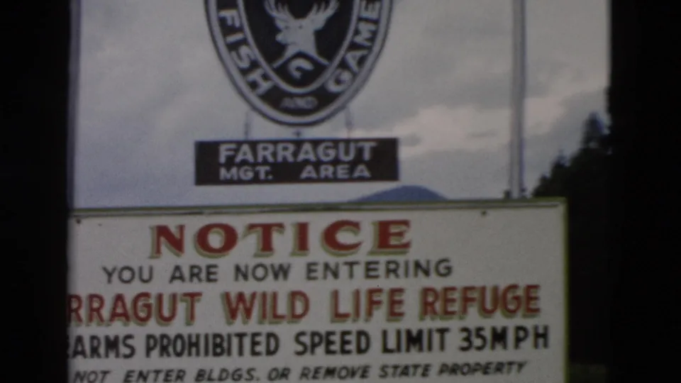 1958 8mm frame of the Farragut Wild Life Refuge entrance notice, with Fish and Game emblem, trees, and cloudy sky visible.