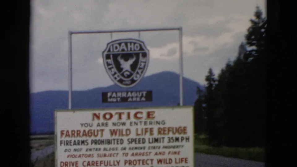 1958 8mm frame showing the Farragut refuge entrance sign from the roadside with forest, mountain backdrop, and cloudy sky.