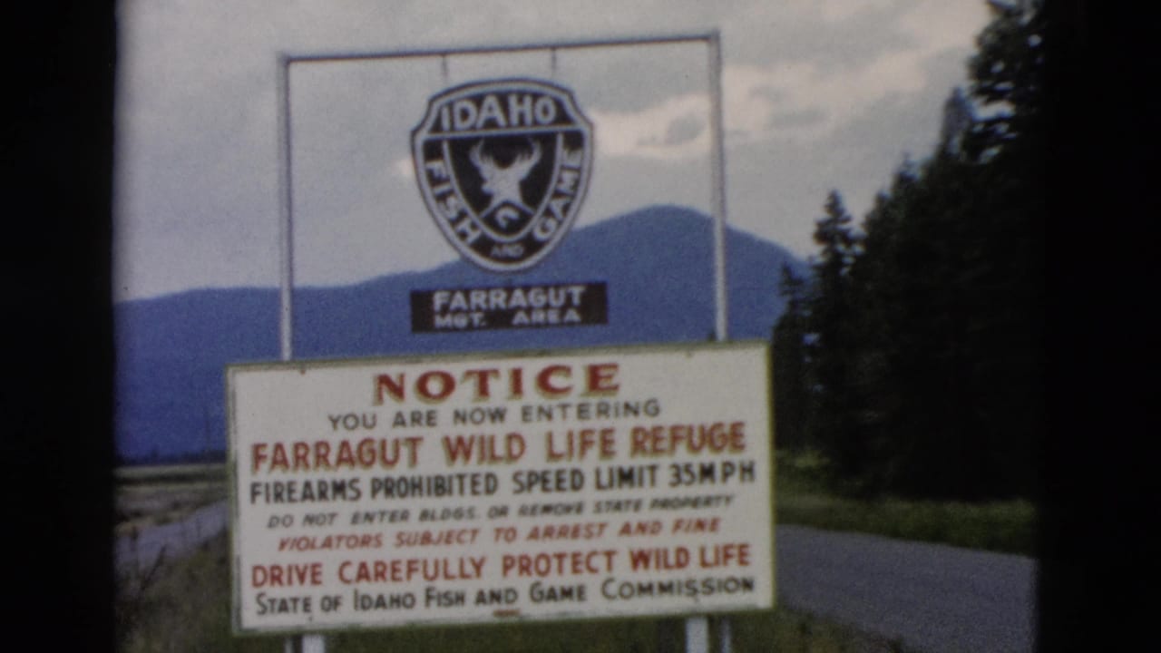 1958 8mm view of the Farragut Wild Life Refuge notice, including firearms and speed limit text, framed by roadside trees and hills.