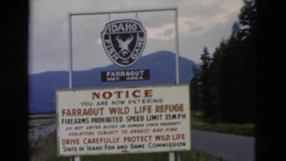 1958 8mm view of the Farragut Wild Life Refuge notice, including firearms and speed limit text, framed by roadside trees and hills.