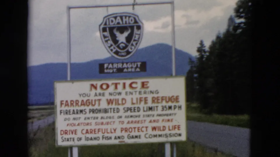 1958 8mm frame centered on the Farragut Wild Life Refuge notice and Idaho Fish and Game emblem against a wooded mountain setting.