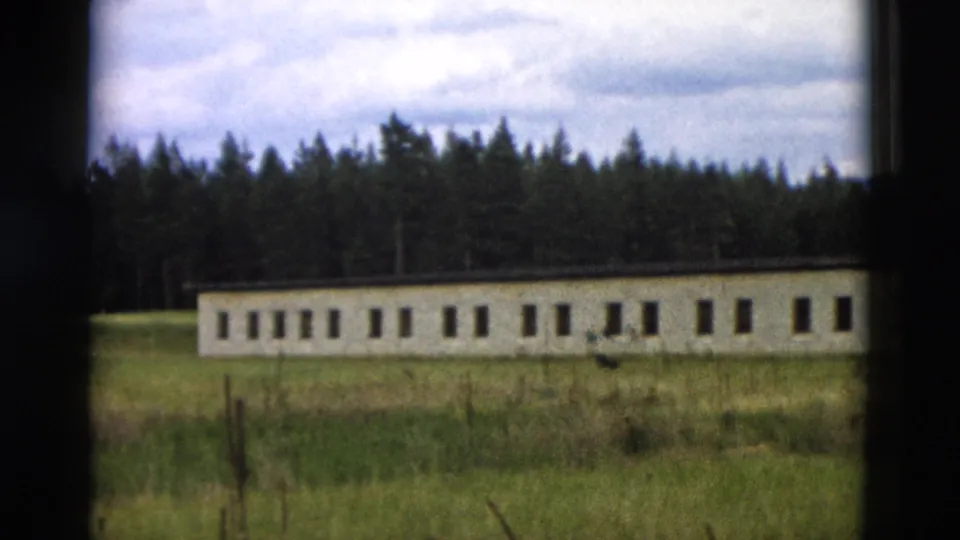 1958 8mm frame showing a long low building in grass near a tree line, likely part of the refuge setting shown in the clip.