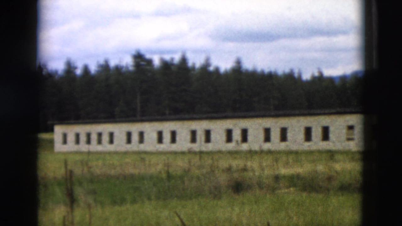 1958 Yellowstone 8mm frame showing a long low building with repeated windows, grass in front, forest behind, and cloudy sky.