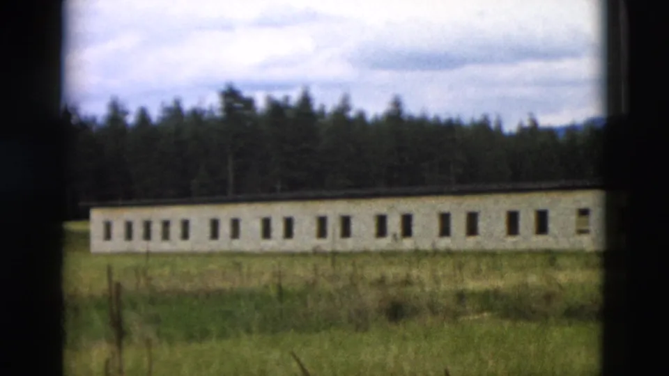 1958 Yellowstone 8mm frame showing a long low building with repeated windows, grass in front, forest behind, and cloudy sky.