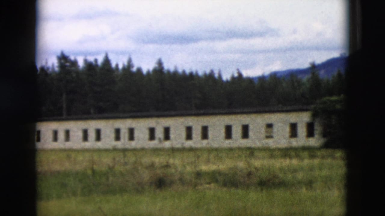 1958 Yellowstone frame of a low institutional-looking building set against forest, with grass in the foreground and hills beyond.