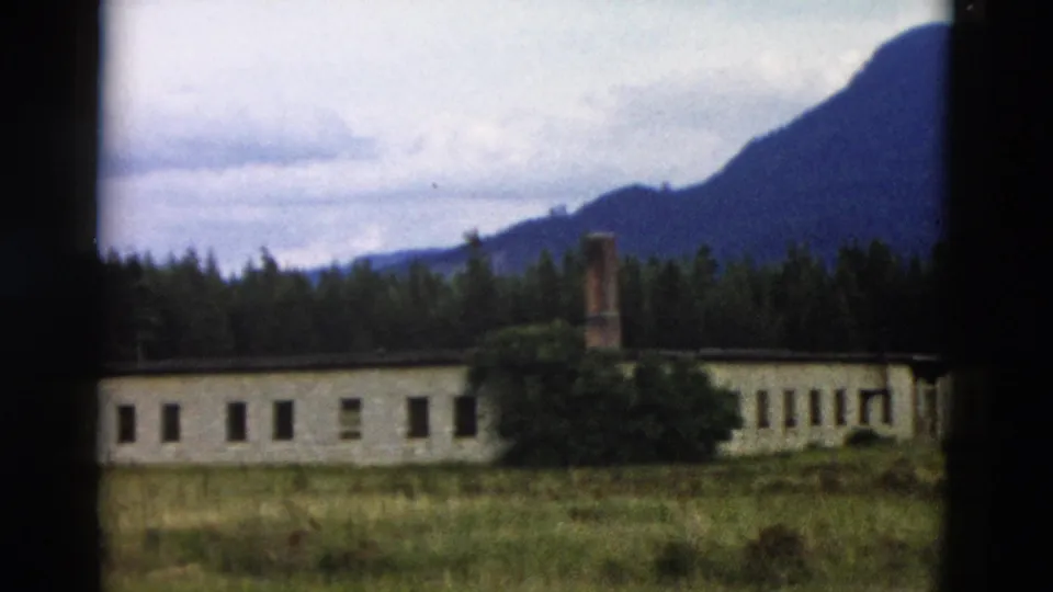Final 1958 Yellowstone frame with the building's right end, brick chimney, foreground grass, dark forest, and mountain backdrop.