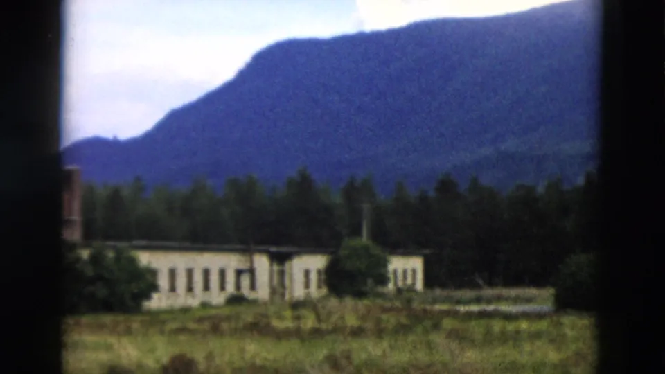 A soft 8mm view of the pale building partly cropped by the frame, with forest and mountain rising beyond.