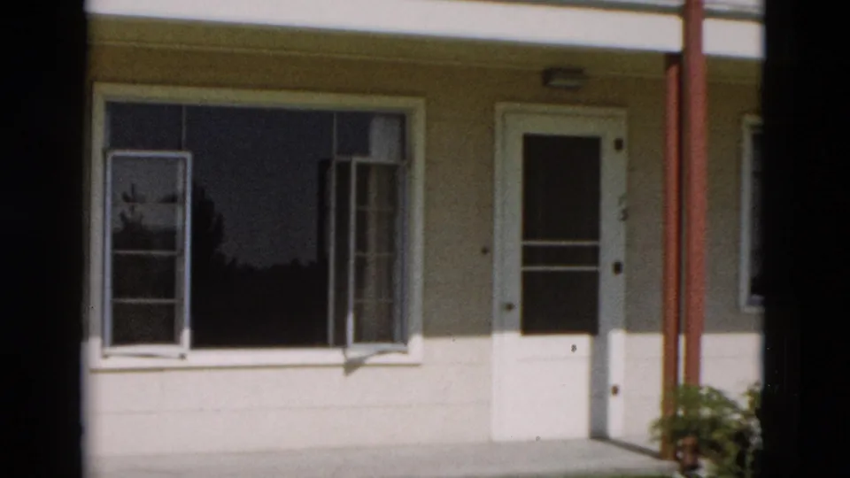 1958 8mm frame from Yellowstone showing a closer pass across an open window, cream siding, red post, and white door edge.