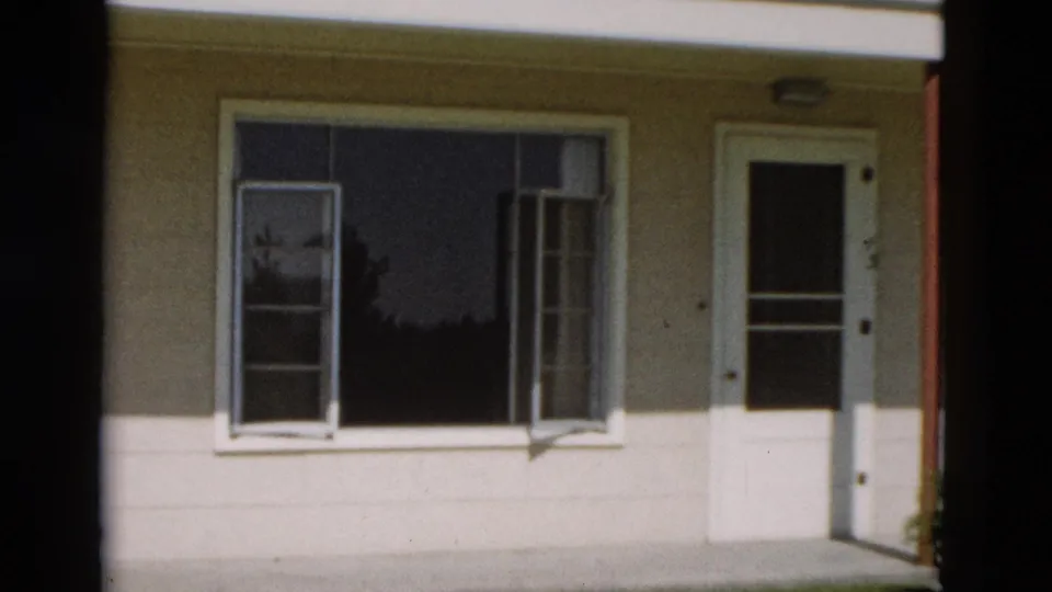1958 Yellowstone, Wyoming home-movie frame showing a modest house facade with open window sashes and a white screen door.