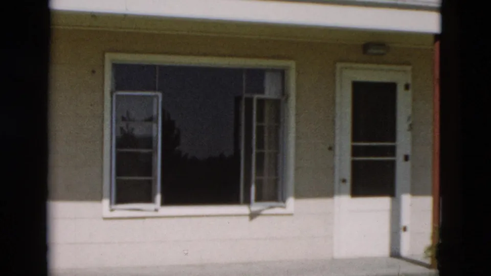 1958 Yellowstone, Wyoming frame of a simple house exterior, with open window sashes beside a white screen door.