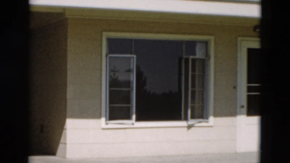 1958 Yellowstone frame of a pale building facade with open casement windows, striped curtains, white trim, and strong shadow.
