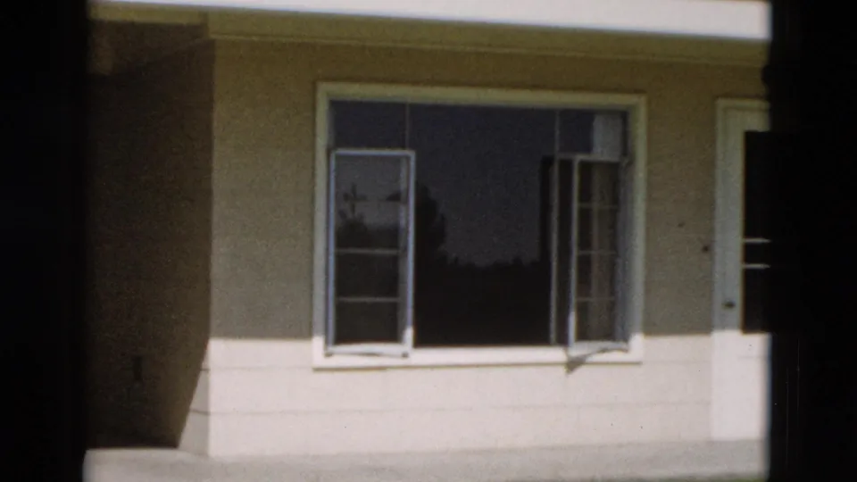 1958 Yellowstone 8mm frame showing open casement windows on a pale exterior wall, with bright sunlight and heavy shadow at the frame edge.