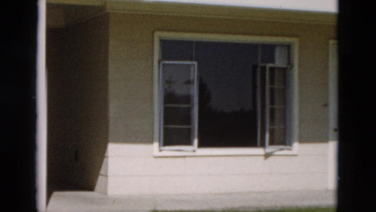 1958 Yellowstone-area home-movie frame showing a pale building wall and open window seen from close range.