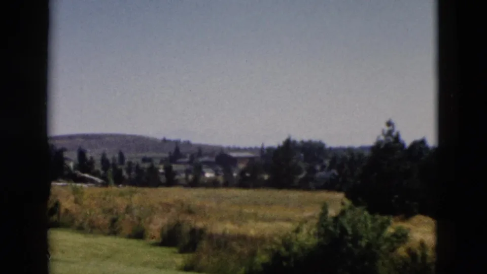 1958 Yellowstone-area 8mm frame showing a grassy plain, distant treeline, low hills, and dark window-like borders.