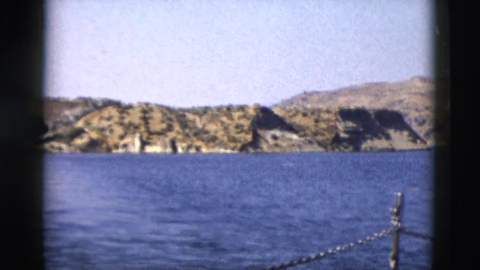 1958 Yellowstone frame showing blue lake ripples, rocky hills, and bright open sky.