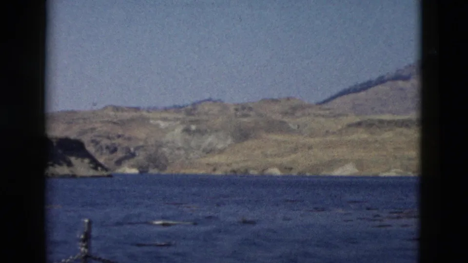 8mm Yellowstone, Wyoming frame showing blue water, distant dry hills, and a partial chain railing from a visitor-shot vessel perspective.