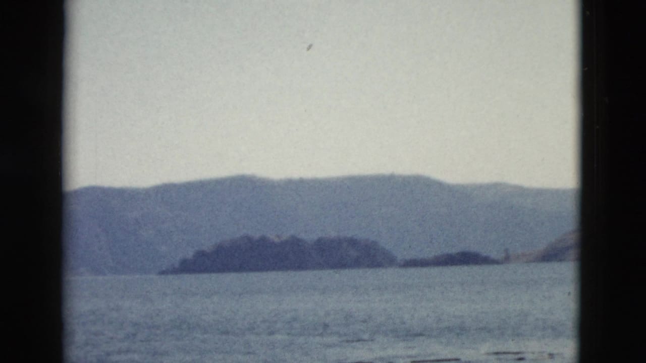 1958 8mm Yellowstone travel footage showing calm water and hazy mountain shoreline from a boat-framed viewpoint.