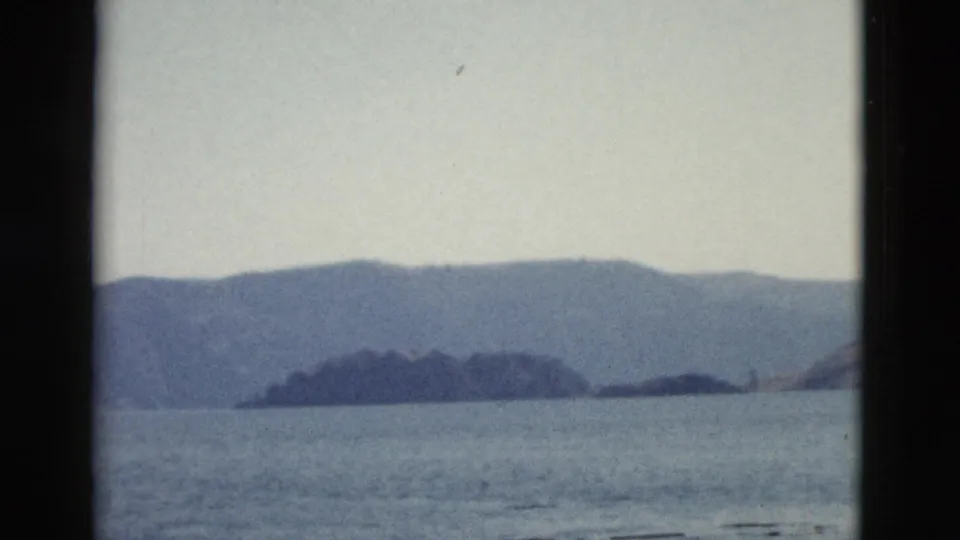 1958 8mm Yellowstone travel footage showing calm water and hazy mountain shoreline from a boat-framed viewpoint.