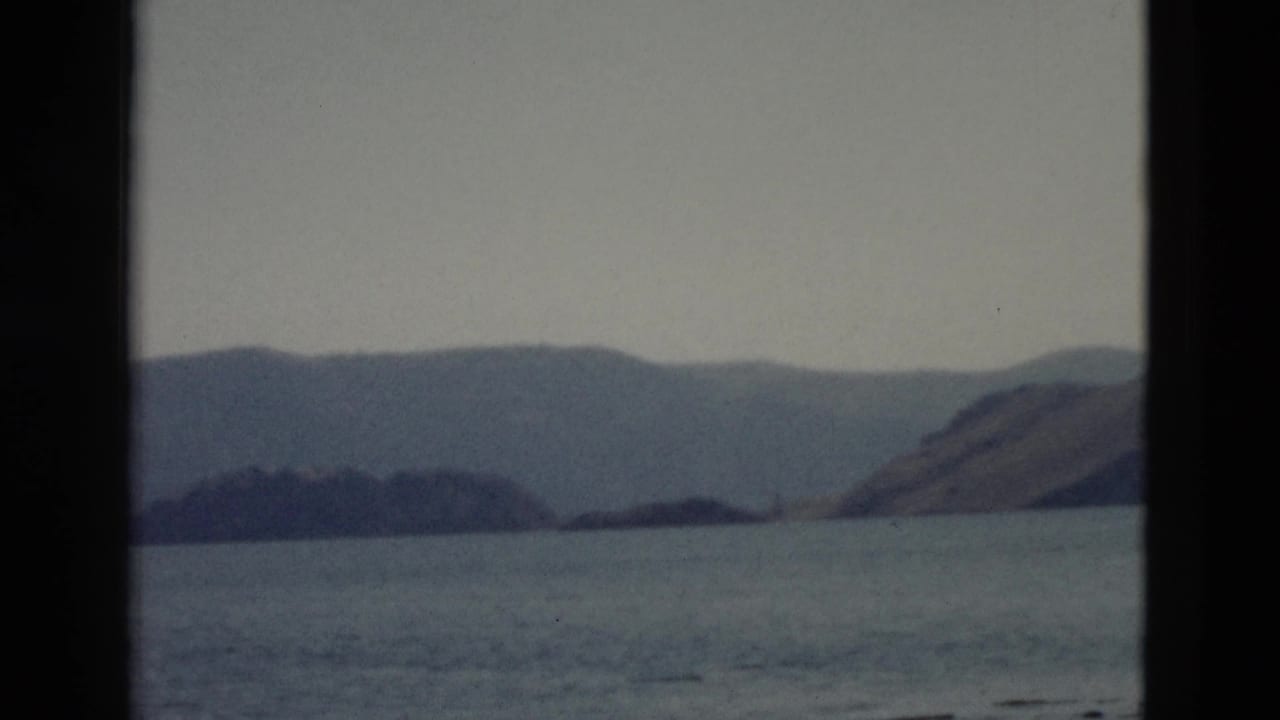 A boat-level view across Yellowstone lake water toward low landforms and distant mountains in faded 8mm color.